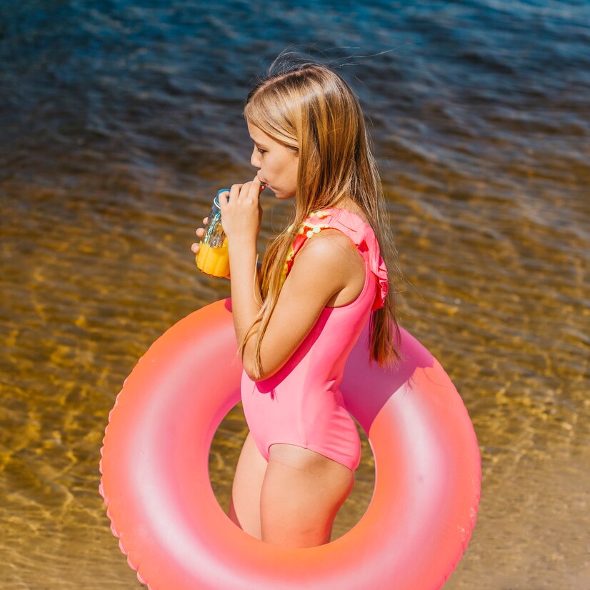 young-girl-swimsuit-with-swimming-ring-drinking-juice-beach_23-2